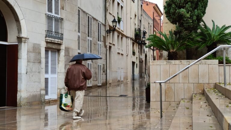 Un ciudadano camina con un paraguas abierto en la plaza de la Església de Vila-seca.
